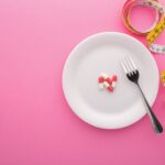dietary-supplement-plate-with-measuring-tape-pink-top-view_104165-230